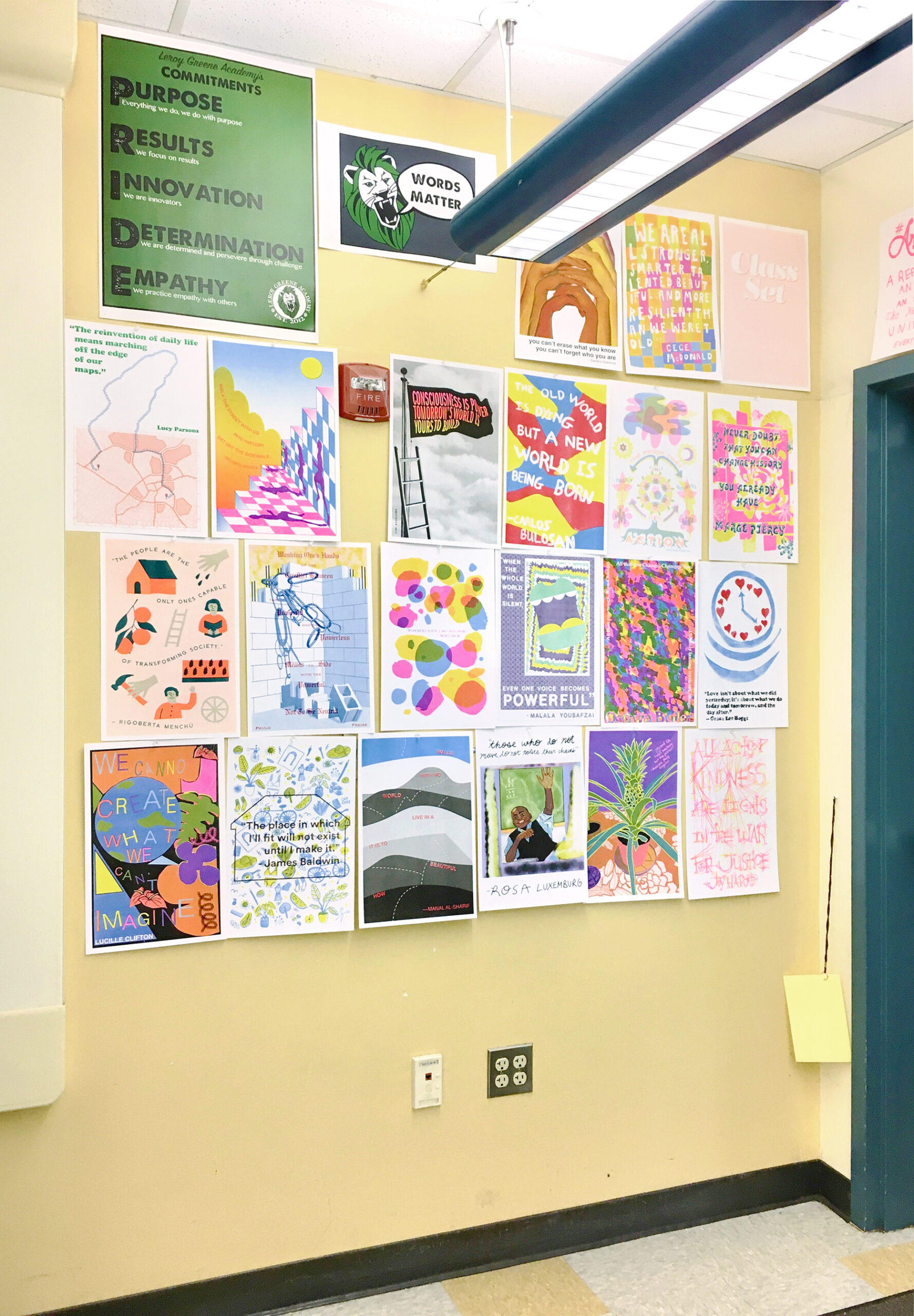 Risograph poster series displayed salon-style on a yellow school hallway wall, arranged in rows beside a green "PRIDE" values poster and a "Words Matter" sign, near a doorway.